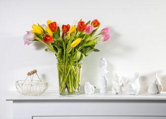 A bouquet of multi-colored tulips in a transparent vase and cup of tea on the white table.