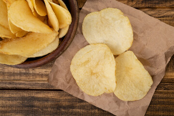 Potato chips in a bowl and on a paper piece over wooden table