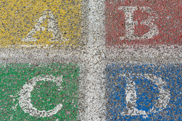 Closeup of A B C D stenciled onto pavement; worn and faded center of a four square court