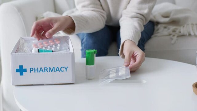 Asian woman receive medication package box free first aid kit from pharmacy hospital delivery service at home in telehealth telemedicine online concept. Check medicine box capsule pack from drugstore.