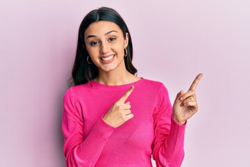 Young hispanic woman wearing casual clothes smiling and looking at the camera pointing with two hands and fingers to the side.