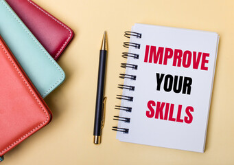 Multi-colored diaries lie on a beige background next to a pen and a notebook with the words IMPROVE YOUR SKILLS. Flat lay.