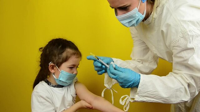 Vaccination of children during the coronavirus pandemic. A doctor vaccinates a little girl during a coronavirus outbreak. Doctor colitis vaccine in child's shoulder on yellow background. Vaccination
