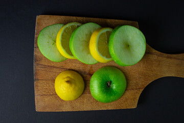 Green apple and lemon on a dark background. Sliced apple and lemon on a black background. Healthy food. Creative photo of fruit