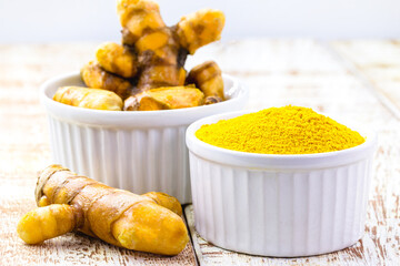 turmeric powder, saffron roots in wooden bowl on white table