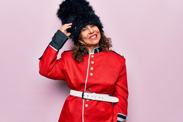 Middle age beautiful wales guard woman wearing traditional uniform over pink background confuse and wonder about question. Uncertain with doubt, thinking with hand on head. Pensive concept.