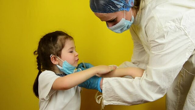 Doctor colitis vaccine in child's shoulder on yellow background.
Vaccination of children during the coronavirus pandemic. A doctor vaccinates a little girl during a coronavirus outbreak.