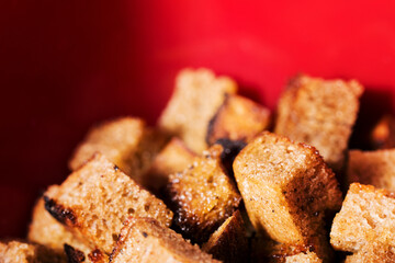 Croutons from black bread on red background. Delicious Fried crunchy crackers. Shallow depth of field image.