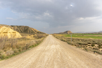 Fototapeta na wymiar gravel road leading into a wild desert landscape under an expressive cloudy sky