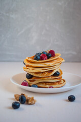 Freshly cooked delicious pancakes with honey, walnut, raspberries and blueberries for breakfast.
