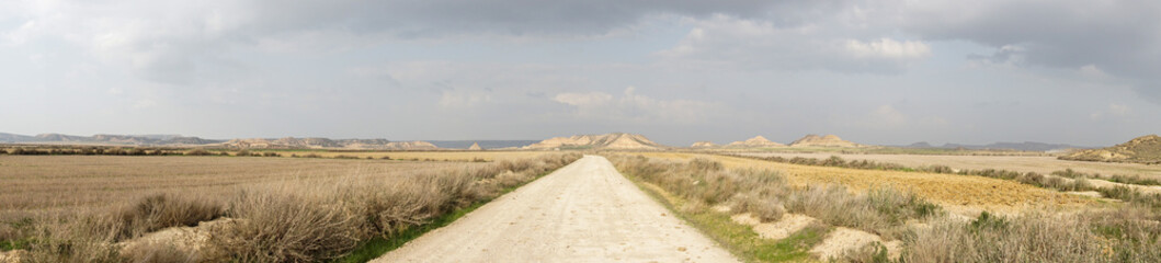 Obraz premium panorama of a gravel road leading into a wild desert landscape under an expressive cloudy sky