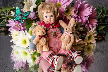 doll sitting on mirror holding teddy bear and stuffed rabbit surrounded by flowers and butterfly