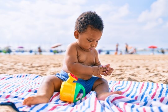 Adorable african american toddler playing with toys sitting on the sand at the beach.