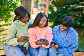 Three african american friends smiling happy using smartphone at the park.