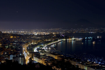 Panorama of the Gulf of Naples at night the metropolitan city with a thousand colors and reflections on the sea and in the background the stars and Vesuvius