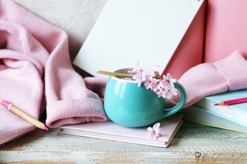 Obraz na płótnie Canvas Cup with water and fresh hyacinth flowers, books, notepads, woolen pink sweater on a light background, at home, romantic congratulation, emotion of love
