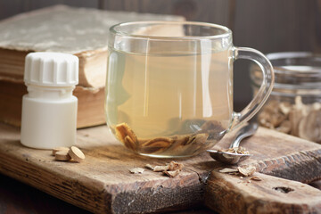 Burdock root tea in a glass cup with dry herb and old apothecary books nearby on wooden rustic background, closeup, naturopathy, natural medicine and homeopathy concept