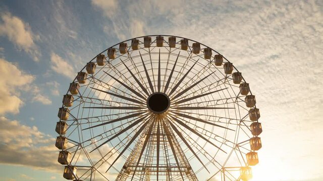 Ferris wheel silhouette at sunset - time lapse - against beautiful clouds in the sky. Big round metal structure (circle) - tall man made construction used for observation and amusement rides in a park