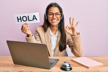 Beautiful hispanic woman wearing operator headset holding hola greenting doing ok sign with fingers, smiling friendly gesturing excellent symbol © Krakenimages.com