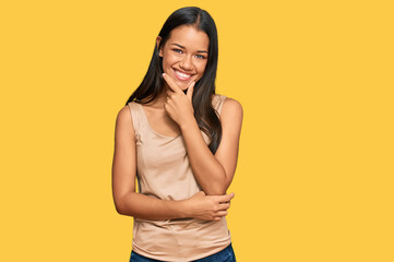 Beautiful hispanic woman wearing casual clothes looking confident at the camera smiling with crossed arms and hand raised on chin. thinking positive.