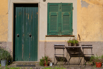Fototapeta na wymiar The decor of the old Italian streets. Green door and shutters. There is a table and chairs under the window.