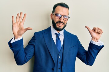 Young man with beard wearing business suit and tie showing and pointing up with fingers number six while smiling confident and happy.