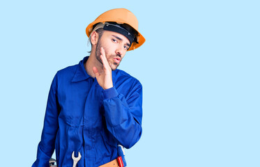 Young hispanic man wearing worker uniform hand on mouth telling secret rumor, whispering malicious talk conversation