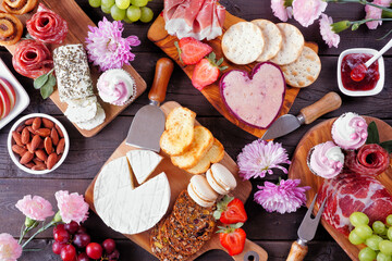 Mother's Day theme charcuterie table scene against a dark wood background. Selection of cheeses,...