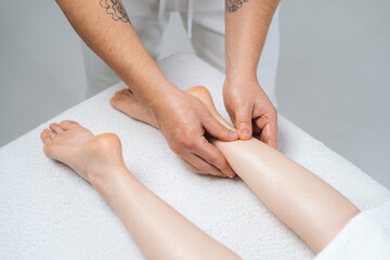 Close-up top view of male masseur with strong hands massaging lower part of leg to young woman lying on massage table on white background. Concept of massage spa treatments