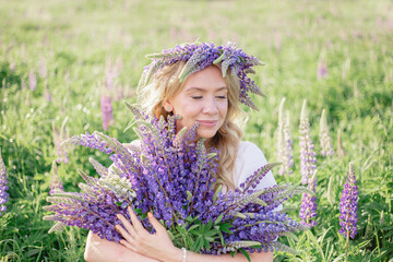 A hippy girl holding bouquet of wildflowers in her hands. Girl hid her face behind bouquet of lupins. Girl holds large bouquet of purple lupins in a flowering field. Nature concept. Present