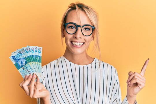 Beautiful blonde woman holding hong kong 20 dollars banknotes smiling happy pointing with hand and finger to the side