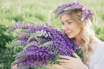 A hippy girl holding bouquet of wildflowers in her hands. Girl hid her face behind bouquet of lupins. Girl holds large bouquet of purple lupins in a flowering field. Nature concept. Present