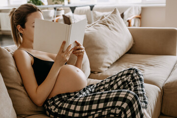Pregnant woman sitting on sofa at home, reading a book.