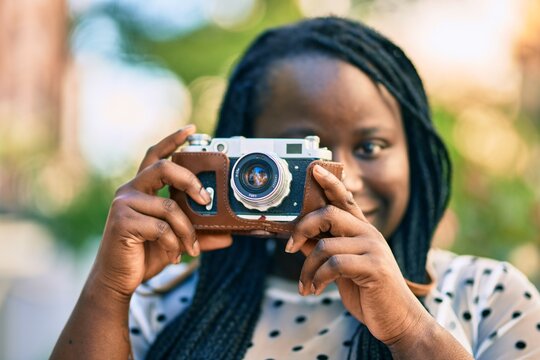 Young african american tourist woman smiling happy using vintage camera at the city.