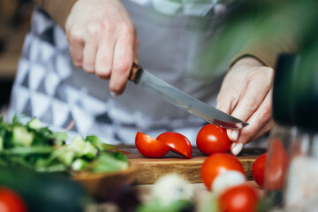 Woman cutting tometoes on wooden board. Close up view.