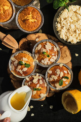 Delicious freshly baked lemon muffins with almond flakes topped with icing, top view. Homemade magdalena on a dark wooden table. The idea of cooking baking for a holiday, layout, vertical frame