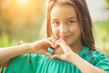 Cute child, little girl showing heart gesture and smiling outdoor. Love summer. Beautiful seven...