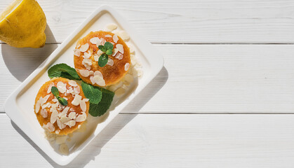 Delicious lemon muffins or cupcake with icing and almond flakes. Homemade magdalena on white wooden background illuminated by sunlight, serving dish idea, top view with copy space.