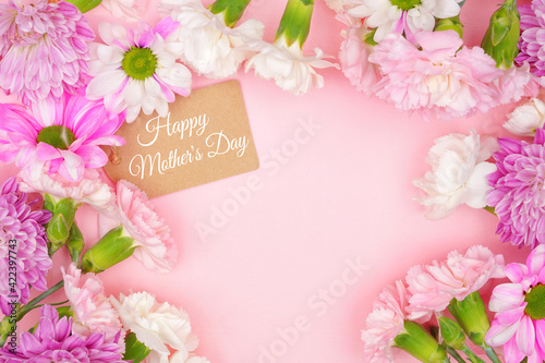 Happy Mothers Day gift tag with frame of pink and white flowers. Top view on a pink background. Copy space.