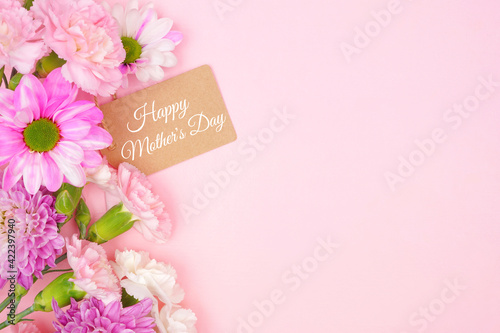 Happy Mothers Day gift tag with side border of pink and white flowers. Top view on a pink background. Copy space.