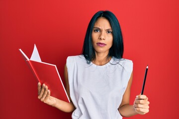 Young african american woman holding book and pencil skeptic and nervous, frowning upset because of problem. negative person.