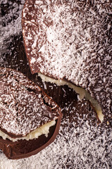 Top view of a cracked chocolate easter egg with coconut filling and grated coconut on the top on a wooden table.