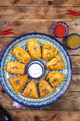 Samsa lies on a platter on a brown wooden background. Fresh baked goods.