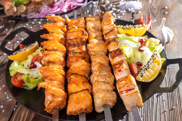 Minced kebab on a metal skewer with sauce, sliced cucumbers, tomatoes and onions.