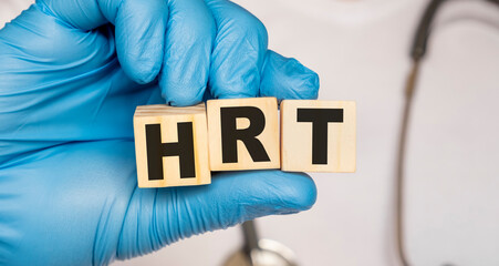HRT Hormone replacement or hormone replacement therapy - word from wooden blocks with letters holding by a doctor's hands in medical protective gloves. Medical concept.