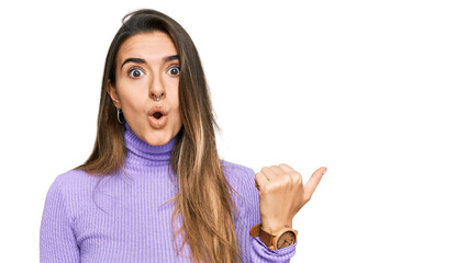 Young hispanic woman wearing casual clothes surprised pointing with hand finger to the side, open...