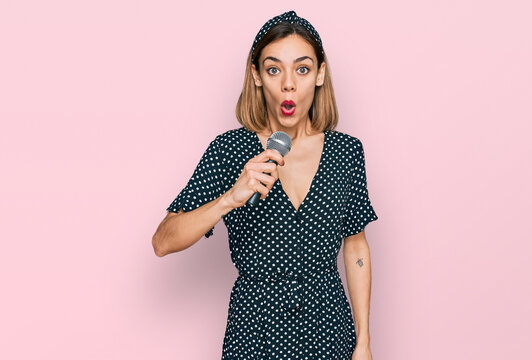 Young blonde girl singing song using microphone scared and amazed with open mouth for surprise, disbelief face