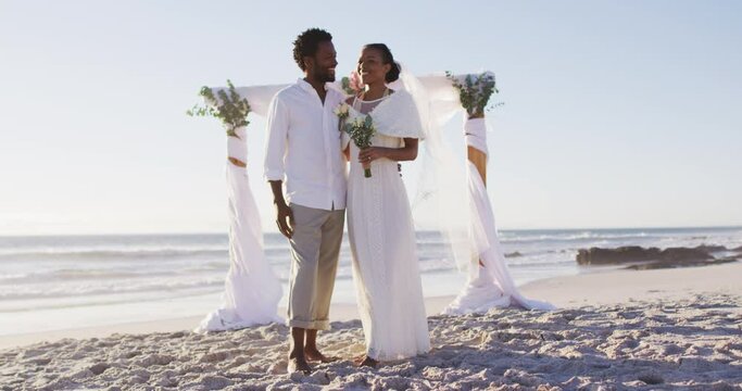 Portrait of african american couple in love getting married and smiling to  camera on the beach