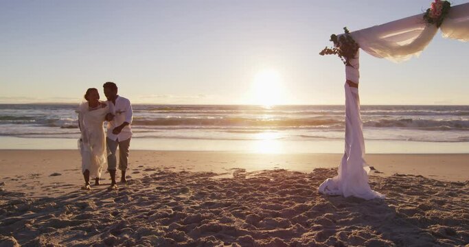African american couple in love getting married, walking on the beach at sunset