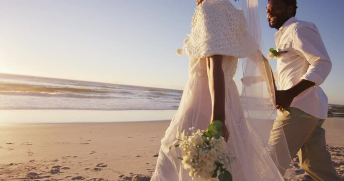 African american couple in love getting married, holding hands on the beach at sunset